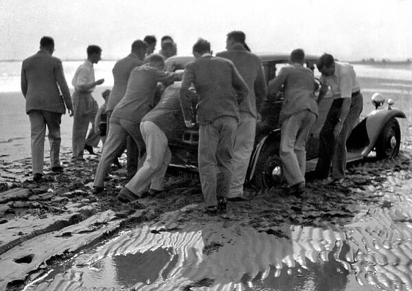 Men pushing car on wet beach