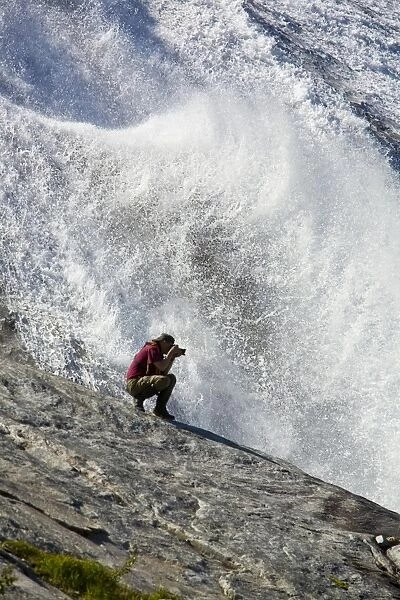 A photographer at a snow melt waterfall in Nordfjord, an arm of the larger Melfjord - situated just above the Arctic Circle - in northern Norway, Barents Sea