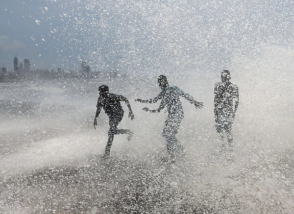 People get drenched by a large wave during high tide at a seafront in Mumbai