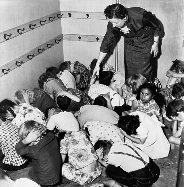 AIR RAID DRILL, 1954. A kindergarten class crouches at the direction of their teacher