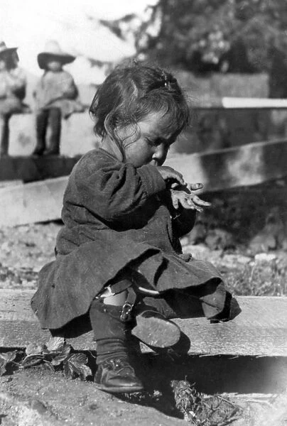 ALASKA: ESKIMO CHILD. A young girl sitting on a wooden plank playing, Alaska. Photograph