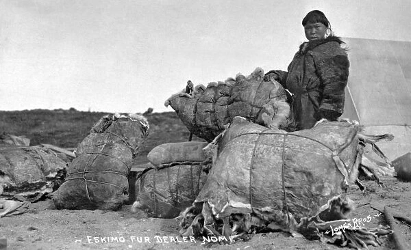 ALASKA: FUR DEALER. An Eskimo fur dealer standing next to several bundles of animal hides