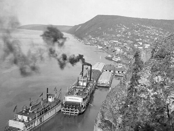 ALASKA: WATERFRONT. Aerial view of riverboats on the Yukon River, cliffs and a