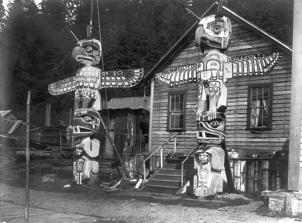 ALERT BAY: VILLAGE, c1914. Two Kwakiutl totem poles in front of a wood frame house