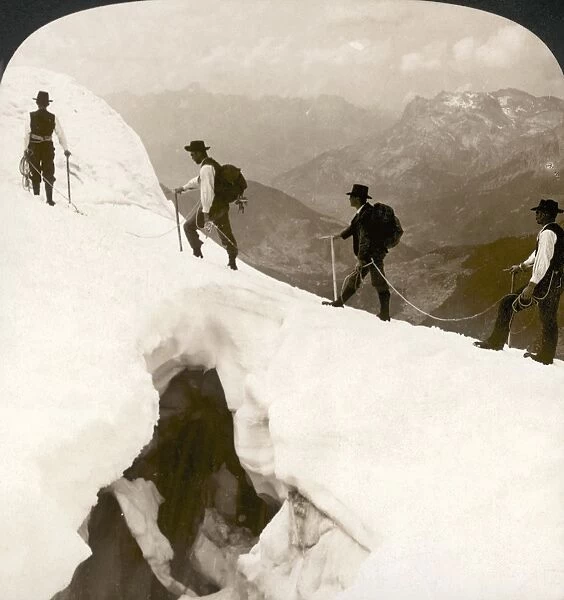 ALPINE MOUNTAINEERING, 1908. Mountain climbers crossing a dangerous crevasse