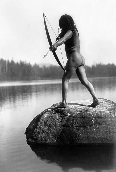 ARCHERY: NOOTKA INDIAN. A nude Nootka Indian bowman taking aim into the water, Pacific Northwest Coast. Photographed by Edward S. Curtis, c1910