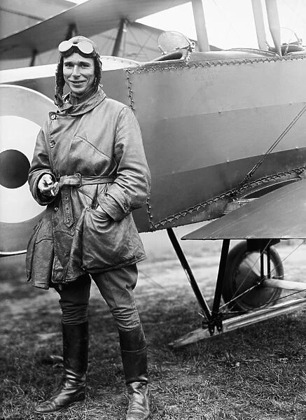 Army aviator wearing flight gear, standing in front of early biplane, c1916-1919