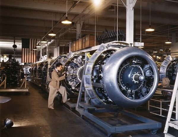 An assembly line worker adding cowlings and control rods to motors for B-25 bomber aircraft at the North American Aviation plant in Inglewood, California, during World War II. Photographed by Alfred T. Palmer, 1942