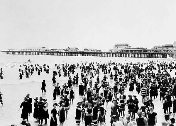 ATLANTIC CITY: BEACH. A crowd of people standing in the ocean with a pier in background