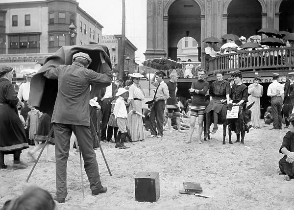 ATLANTIC CITY: BEACH. A photographer on a crowded beach taking a picture of a group of three people with a donkey (including a woman with a sign saying I could stay in Atlantic City forever, Atlantic City, New Jersey. Photograph, late 19th or early 20th century