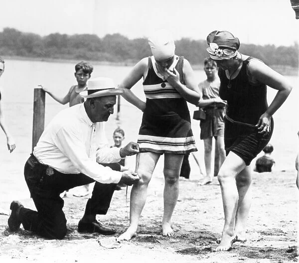 BATHING SUITS, 1922. A Public Buildings and Grounds officer measures womens bathing suits to ensure they are not more than six inches above the knee, Washington, D. C. 1922
