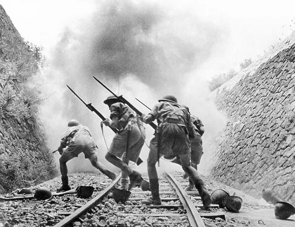 With bayonets fixed to their rifles, soldiers of the British Eighth Army advance through a disused rail cutting to take a railway strongpoint in Sicily, August 1943