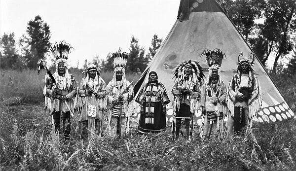 BLACKFOOT SINGERS, c1913. A group of Blackfoot men and one woman singing in front of a tepee. Photograph, c1913