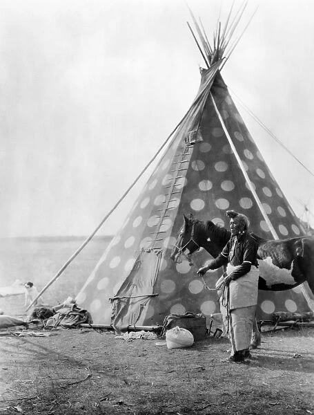 BLACKFOOT TEPEE, c1927. A Blackfoot Native American holding a horse outside a painted tepee. Photograph by Edward Curtis, c1927