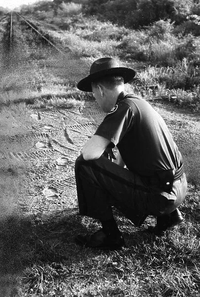 BORDER PATROL INSPECTOR. An American Border Patrol Inspector reads tracks left by illegal immigrants. Photograph, 1957