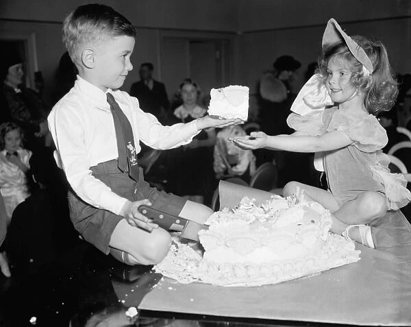 A boy and girl sharing a slice of cake while sitting on a table top at the National Childrens Frolic N. B. C. Party in New York City. Photographed on 19 March 1938