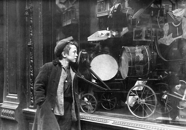 A boy looking at Christmas toys in a shop window. Photograph, early 20th century