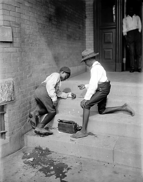 BOYS SHOOTING CRAPS, c1901. Two African American boys gambling with dice on a stoop