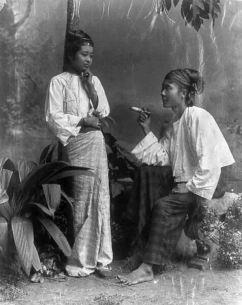 BURMA: WOMEN. Two Burmese women, one standing and one seated, smoking a cigar. Photograph