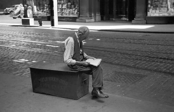 BUSINESS MAN, 1940. A businessman sitting on a garbage crate reading while waiting