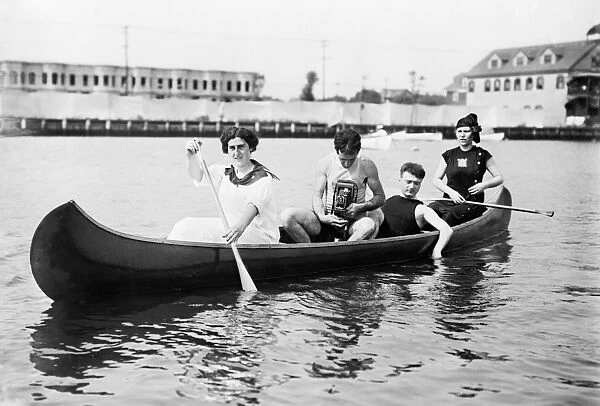 CANOE, c1910. Two women paddling a canoe with two men, one holding a camera. Photograph