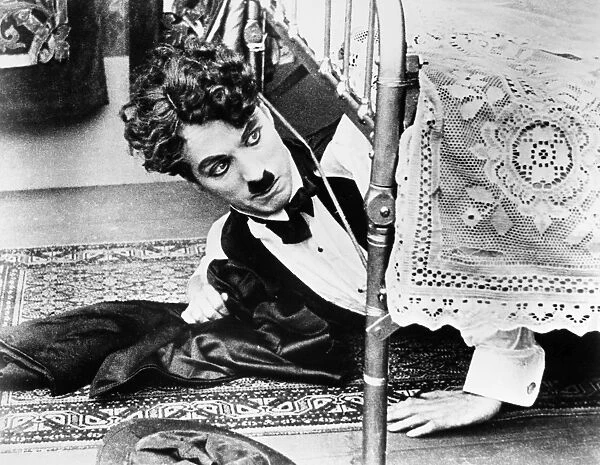 CHARLIE CHAPLIN (1889-1977). Charles Spencer Chaplin. English comedian. Getting out from under the bed in one of his silent movies from the 1920s