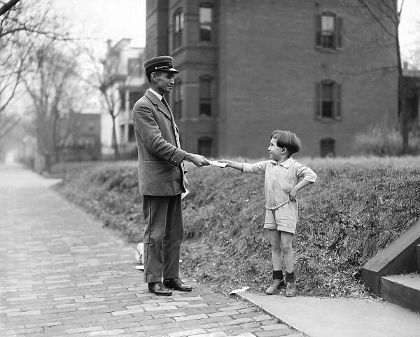 CHRISTMAS, 1920. A boy handing a mail carrier a letter for Santa Claus. Photograph