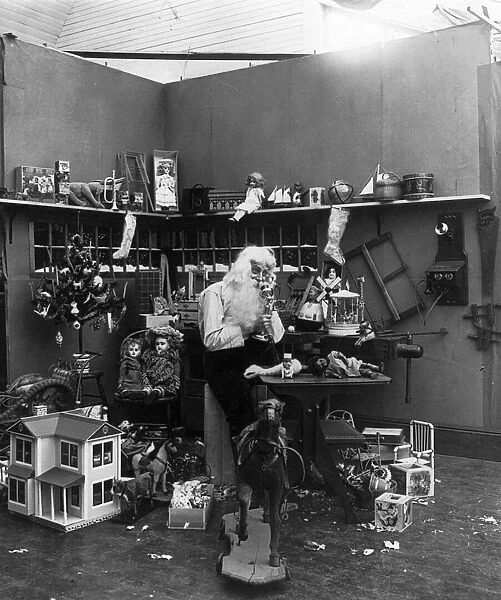 CHRISTMAS EVE, c1906. A studio photograph of Santa Claus in his workshop speaking on a telephone