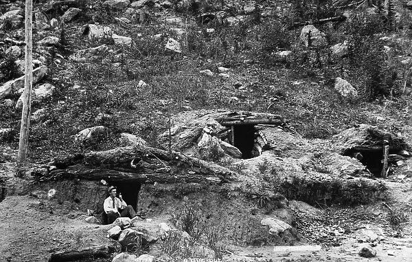 COLORADO: DUGOUT HOME. A man seated outside a dugout cabin at the side of a hill