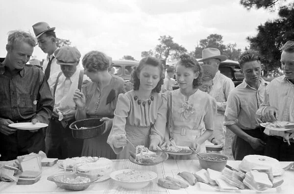 COMMUNITY DINNER, 1940. Men and women serving themselves dinner at the all-day