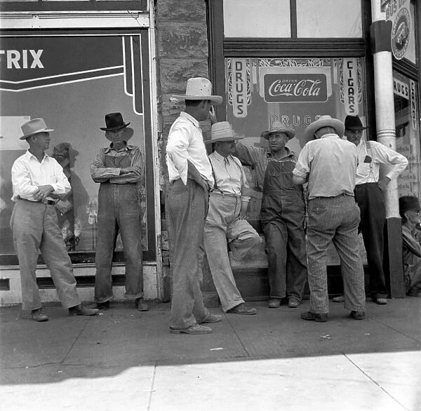 DROUGHT FARMERS, 1936. Drought farmers line the shady side of a street in a town