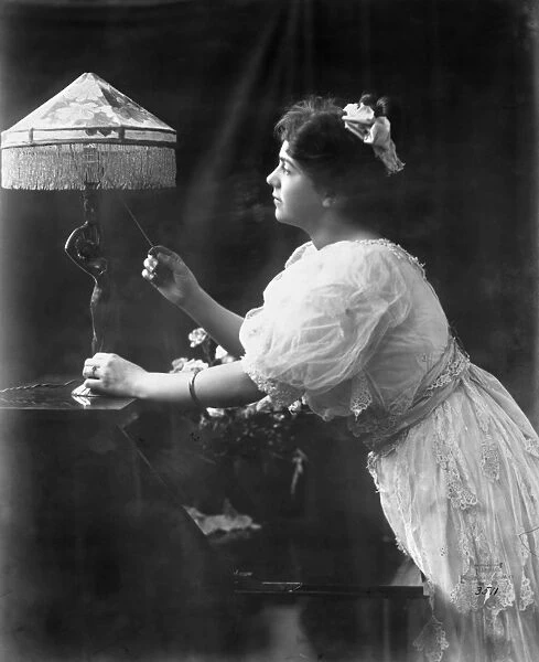 ELECTRIC LAMP, 1908. A woman pulling the switch on an electric lamp, which has