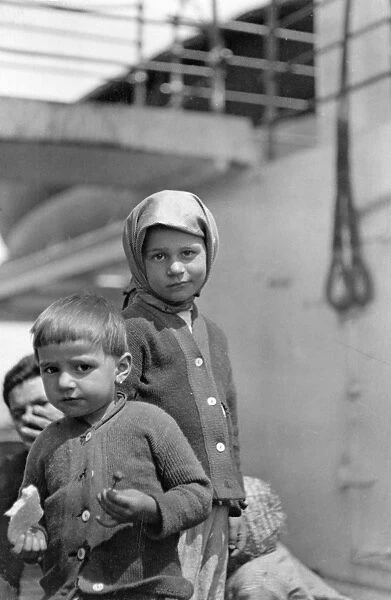 ELLIS ISLAND: IMMIGRANTS. Young boy and girl standing before a steamer at Ellis Island