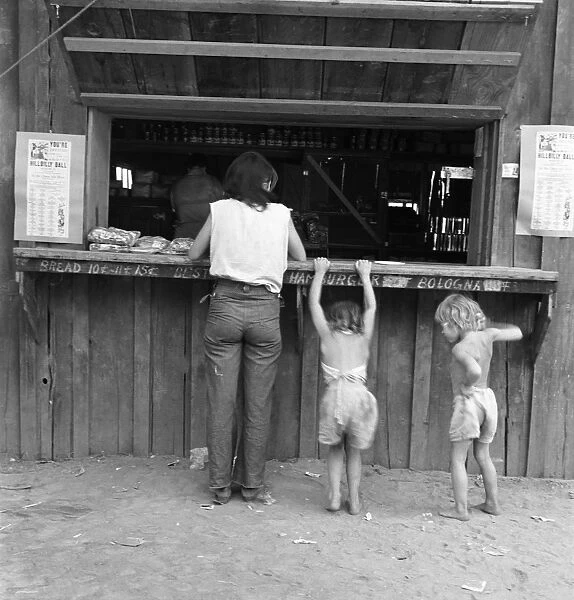 FOOD STAND, 1939. A migrant hop picker and her two children at the window of a