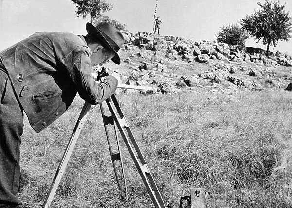 A geologist (foreground) searches for an oil deposit in an American field with the help of his rod man. Photographed c1944