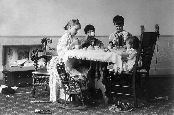 Four girls having a tea party around a table. Photograph, c1893