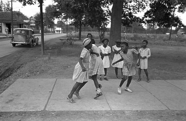 GIRLS PLAYING, 1938. A group of African American girls playing on a rural sidewalk in Lafayette