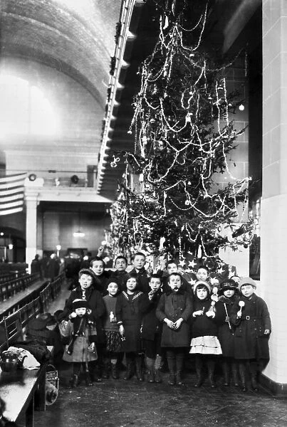 Group of immigrant children photographed in front of a Christmas tree inside the registry room at Ellis Island, New York City, 1920
