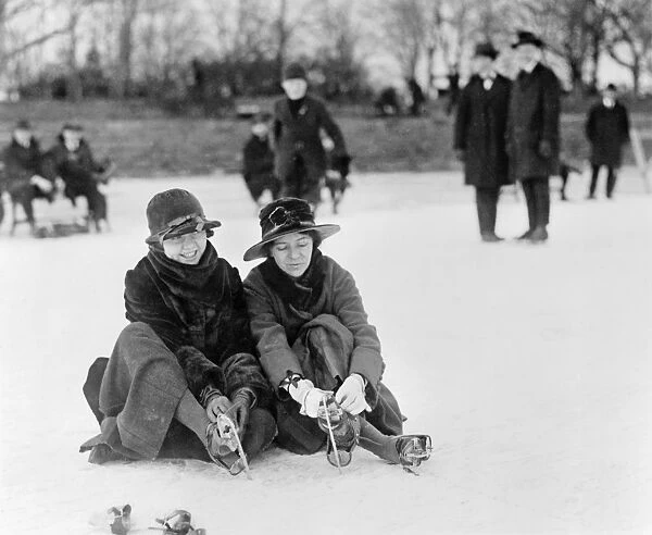 ICE SKATING, c1915. Two women seated on the snow putting on their ice skates, in the Washington
