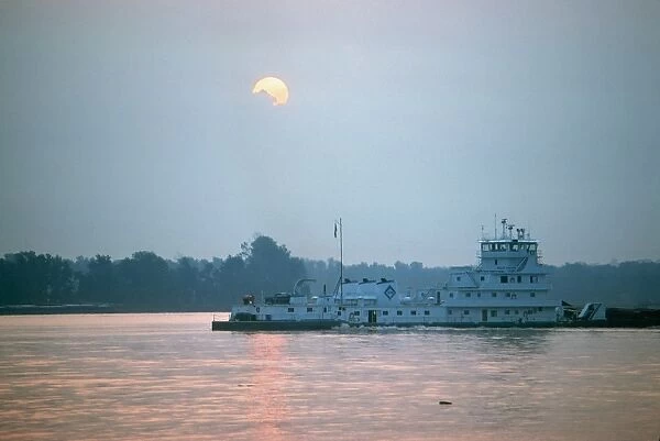 ILLINOIS: TOWBOAT. The Sally Archer, a towboat of the Archer Daniels Midland Company, pushing a barge at the confluence of the Ohio and Mississippi Rivers at Cairo, Illinois, at sunrise. Photographed c1974