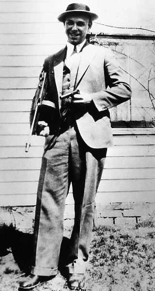 JOHN DILLINGER (1903-1934). American bank robber. Photographed in 1934 at his fathers home in Mooresville, Indiana, holding a submachine gun and the wooden gun that he claimed he used to escaspe from jail in Crown Point, Indiana