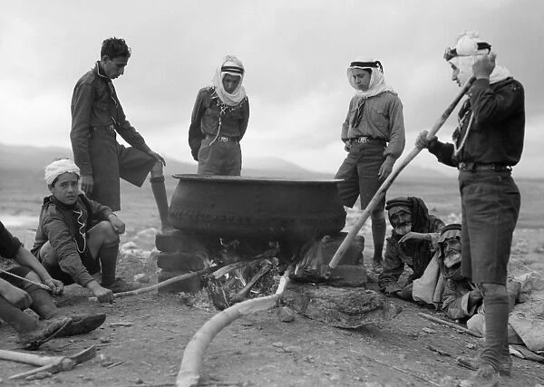 JORDAN: BEDOUINS, 1935. A group of Bedouins cooking in a large pot, in the Shunat