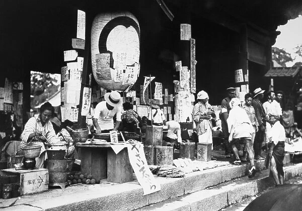 A makeshift food market at the gate of a Buddhist temple in or near Tokyo, Japan, in the aftermath of the great earthquake that struck the Kanto plain on 1 September 1923. Columns and a large lantern are covered with posters sharing and seeking information about people