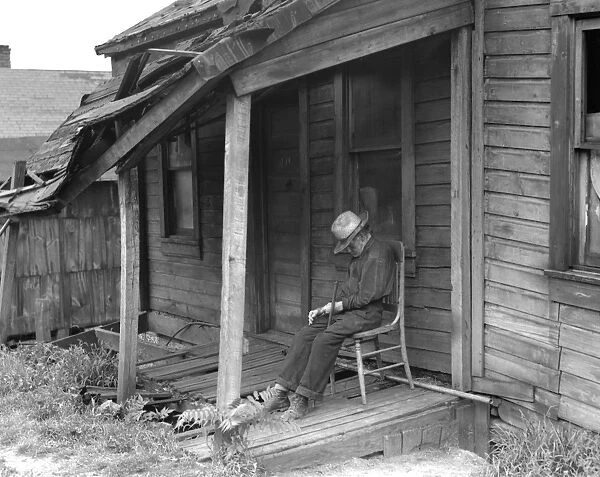 MAN ON PORCH, 1936. Old Age. Old man taking a nap on the dilapidated porch of a run down home