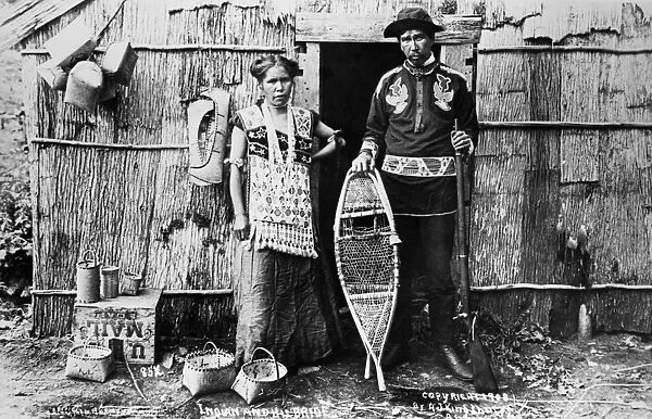 MENOMINEE COUPLE, 1908. A Menominee Native American couple standing outside a bark