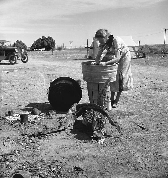 MIGRANT CAMP, 1937. A woman washing clothes in a washbin at a camp for migrant