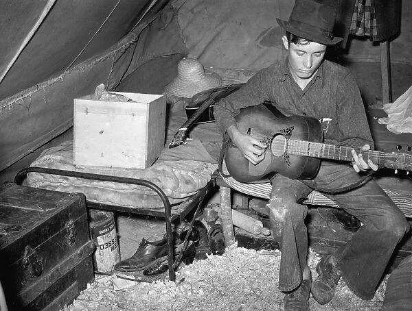 MIGRANT FARMER, 1939. A migrant strawberry picker playing guitar in his tent near Hammond
