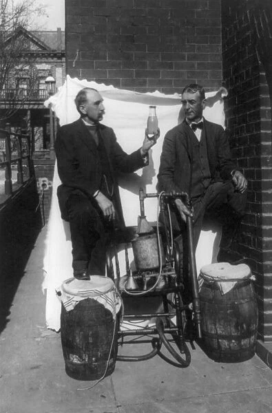 MOONSHINE, 1920s. Two men standing with a small distillery and a bottle of moonshine