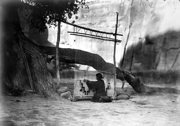 NAVAJO WEAVER, c1905. A Navajo woman weaving a blanket under a cottonwood tree, with a canyon wall in the background. Photograph by Edward Curtis, c1905