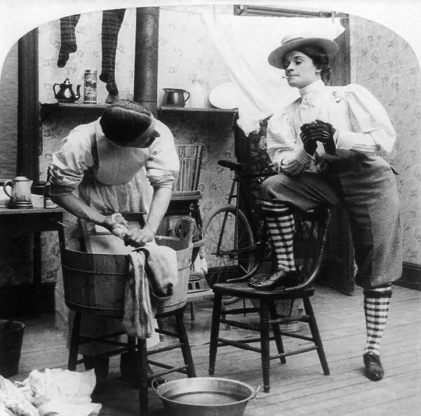 THE NEW WOMAN, c1897. A woman wearing knickers and smoking a cigarette watches a man washing laundry in a tub. American stereograph, c1897